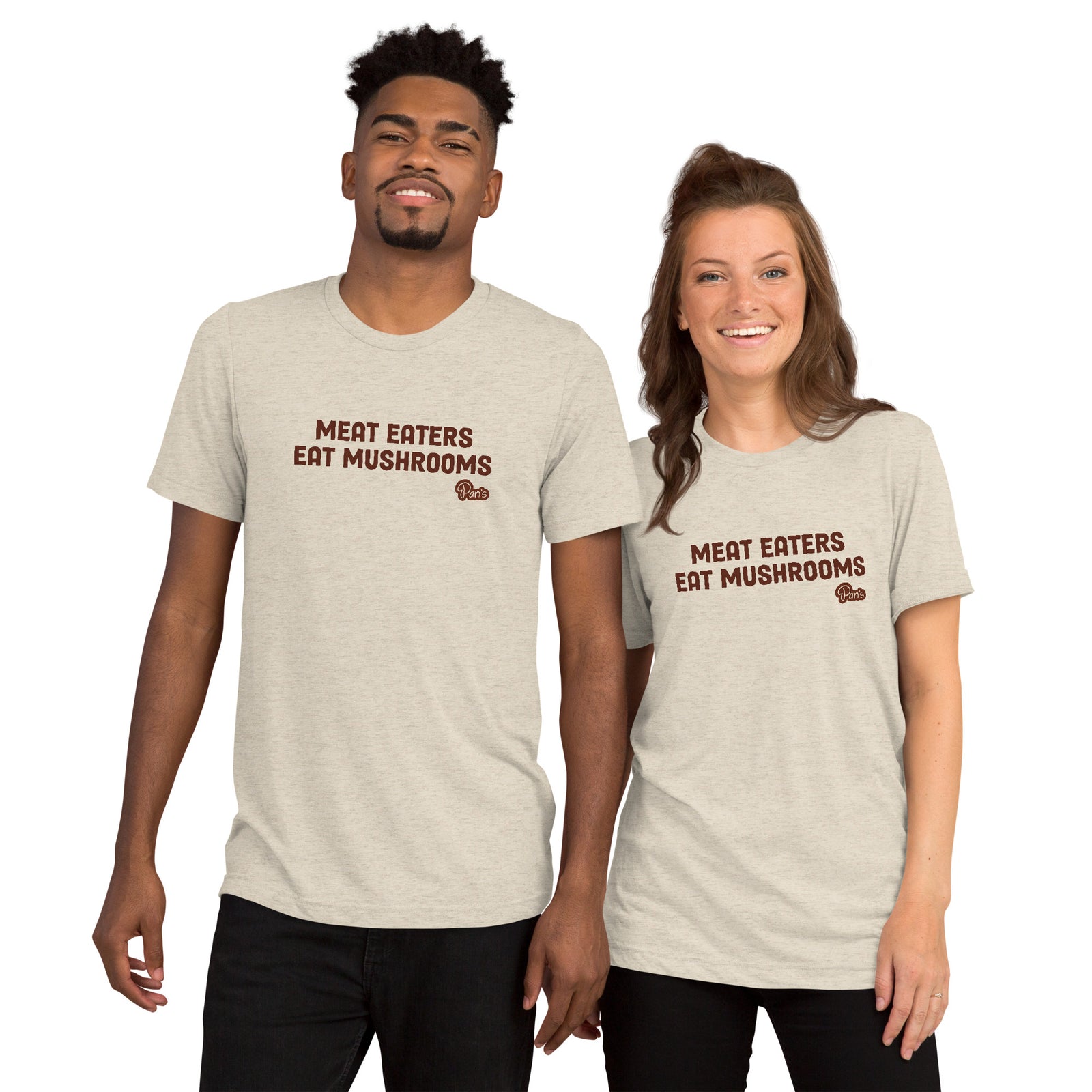 Front view of man and woman wearing heather beige t-shirt that says "Meat Eaters Eat Mushrooms" and the Pan's logo beneath. 